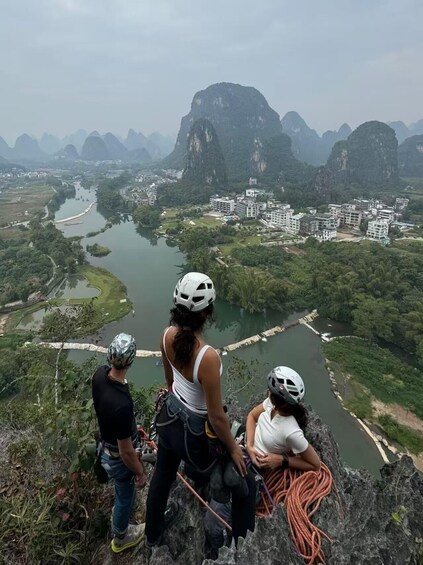 Three people on a rocky overlook with a river and buildings in the background. 4