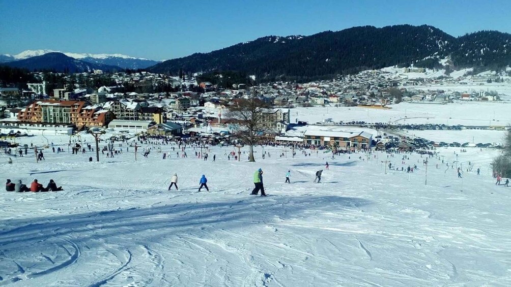 A snowy ski resort with skiers and snowboarders, buildings, and mountains in the background. 4
