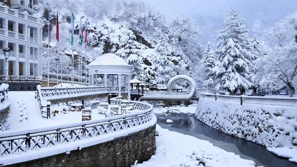 A snow-covered park with a gazebo, benches, and a circular water feature. 5