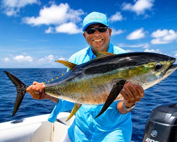 A person holding a large fish on a boat with a clear blue sky in the background. 1