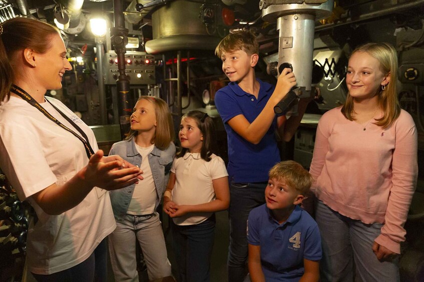 A group of people in a metallic industrial setting with machinery and pipes. 5