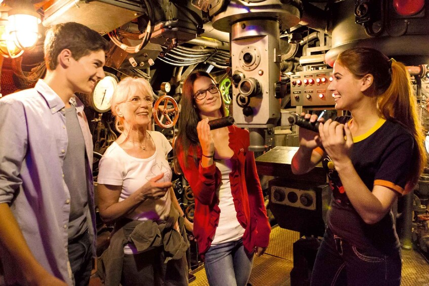 A group of people in a room with industrial machinery and gauges. 2