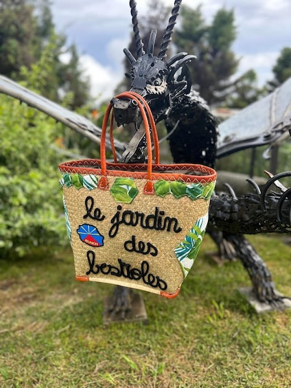 A wicker basket with a handle, decorated with green leaves and a blue fish, hanging from a metal structure. 1