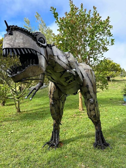A dinosaur sculpture in a grassy field with trees in the background. 5