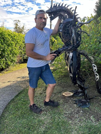 A man standing next to a large mechanical sculpture outdoors. 3