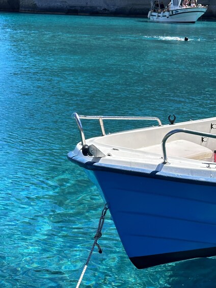 A blue boat tied to a dock with clear turquoise water and a rocky shoreline in the background. 5