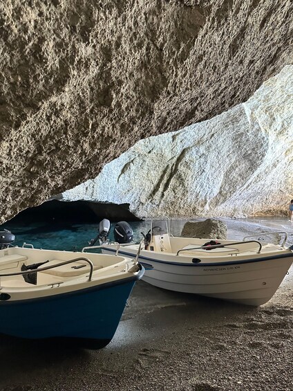 Two boats docked at a rocky beach with a cave entrance. 3