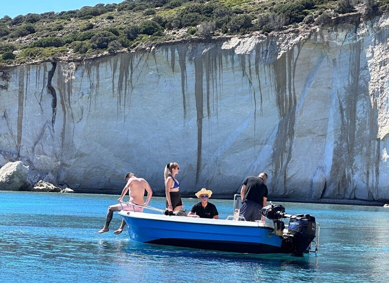 A small boat with people on a clear blue sea, surrounded by cliffs. 1