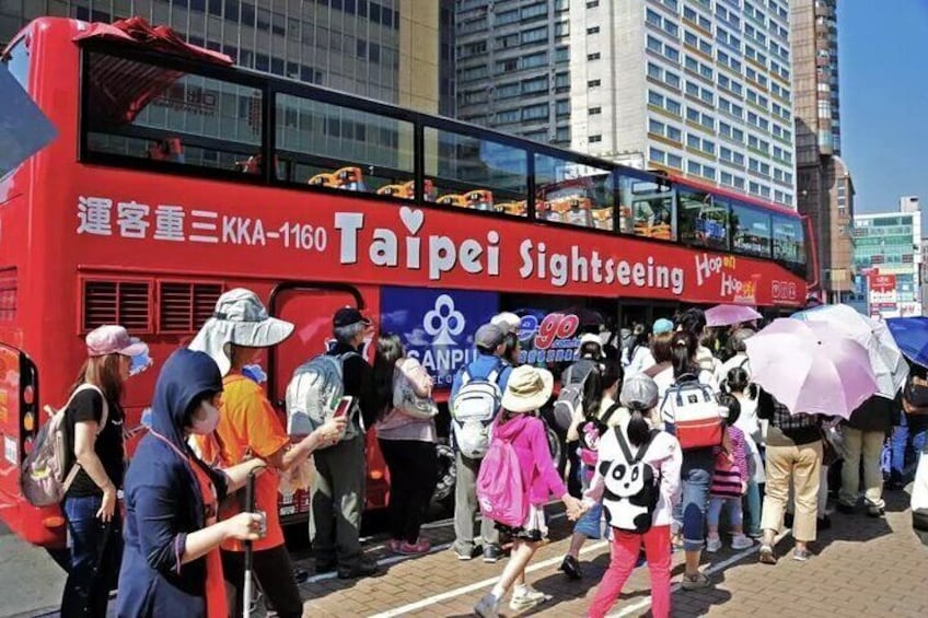 A red double-decker bus with 'Taipei Sightseeing' written on it, surrounded by people. 4