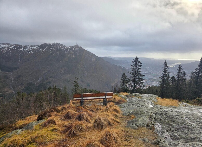 A bench on a rocky outcrop overlooking a mountainous landscape with a distant town. 2