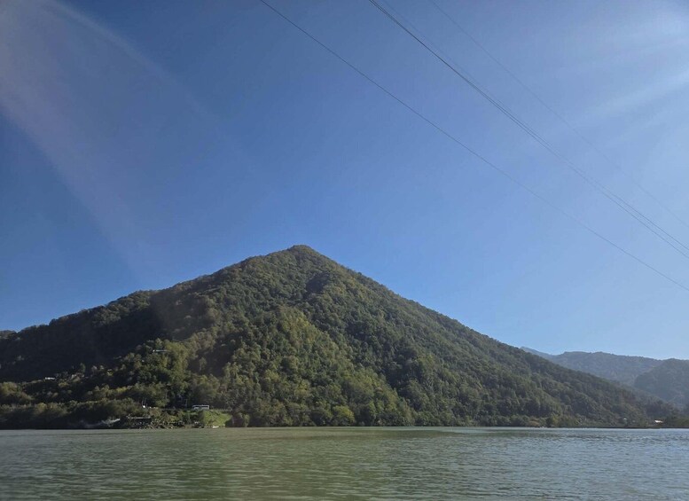 A mountain with dense forest, a body of water in the foreground, and power lines in the sky. 4