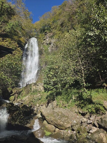 A waterfall cascading over rocks, surrounded by lush greenery and a stone bridge. 1
