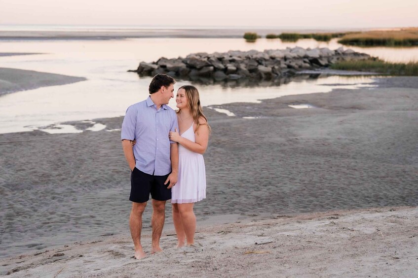 A couple standing on a sandy beach with a rocky shoreline and calm water in the background. 5