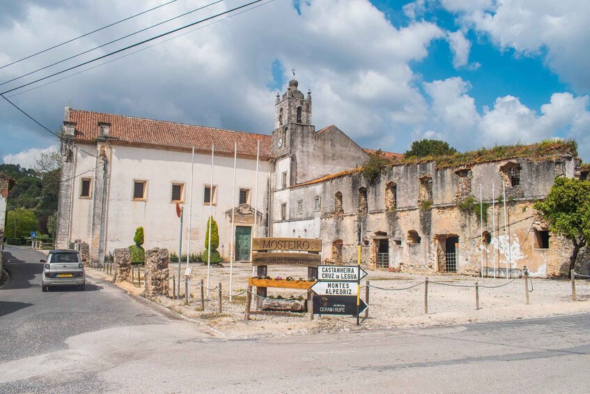 A historic building with a clock tower, a signpost with directions to local attractions, and a car parked on the street. 4