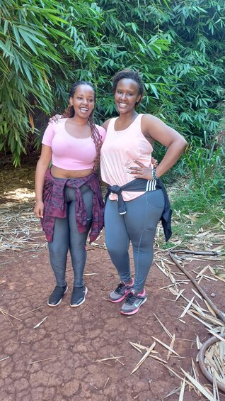 Two people standing outdoors with greenery in the background. 5