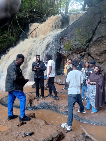 A group of people standing on rocks near a waterfall. 1