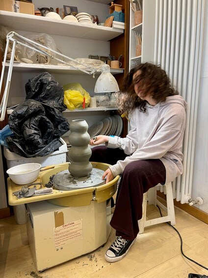 A person working on pottery at a wheel, surrounded by pottery tools and materials. 2