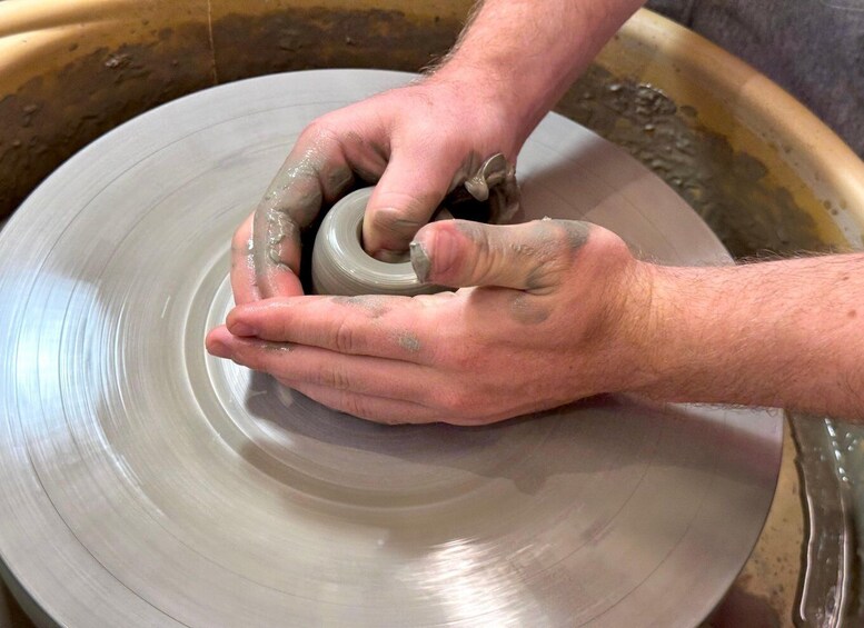 Hands shaping a clay pot on a spinning wheel. 1