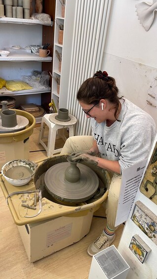 A person working on a pottery wheel, surrounded by pottery tools and materials. 5