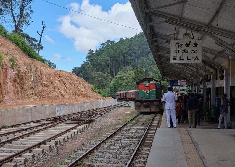 A train at a station with a sign reading 'ELLA' and people waiting on the platform. 3