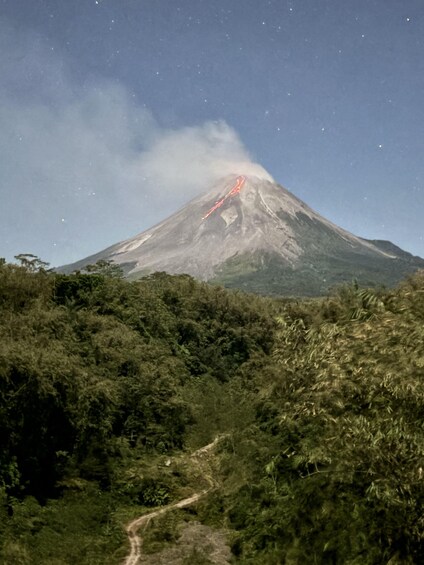Un vulcano con colate laviche attive, circondato da una fitta foresta e un cielo sereno. 2