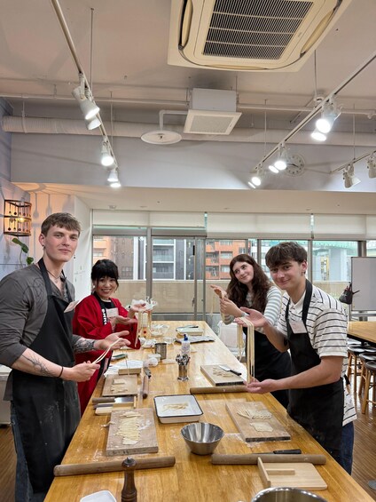 A group of people engaged in a cooking class, with cooking utensils and ingredients on a long wooden table. 4