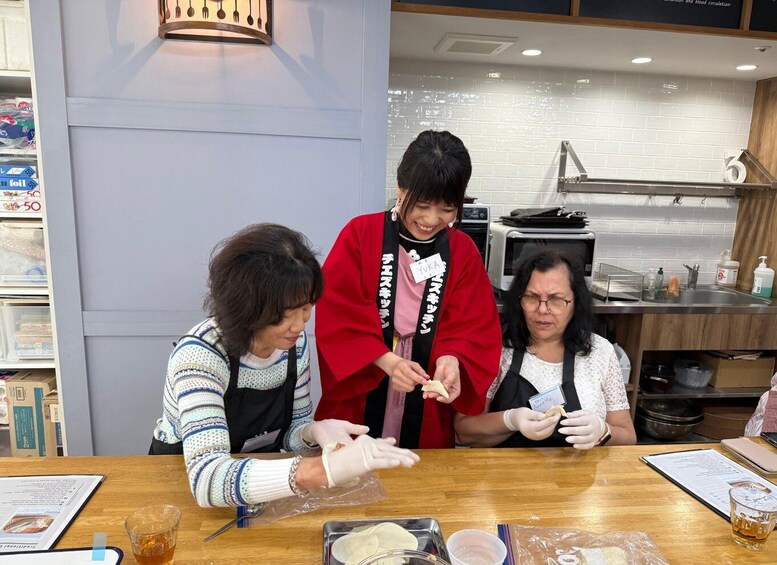 Three people at a counter, one wearing a red coat, preparing food. 3