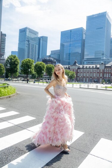 A person in a pink feathered dress standing on a pedestrian crossing in an urban area with modern buildings and trees in the background. 4