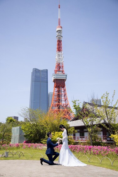 A couple in a park with a tall tower in the background. 1