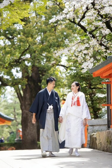 Two individuals in traditional attire walking on a path with cherry blossoms and a traditional building in the background. 5
