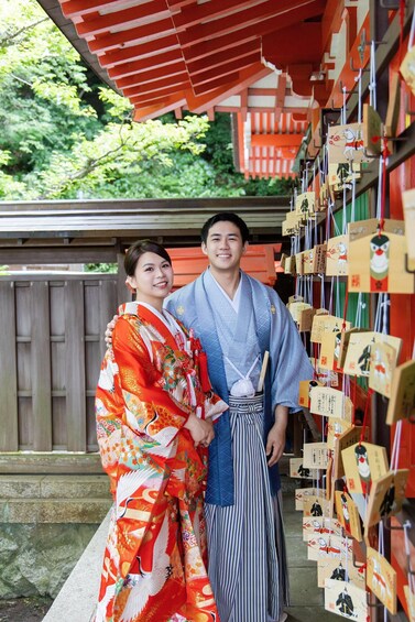 Two people in traditional Japanese attire standing in front of a shrine with wooden plaques. 4