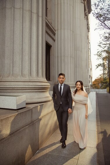 A man and a woman walking on a sidewalk in front of a classical building with large columns. 5