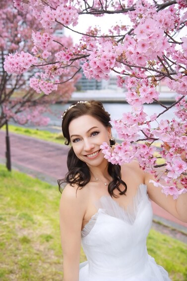 A person in a white dress with a tiara, standing under cherry blossoms. 2