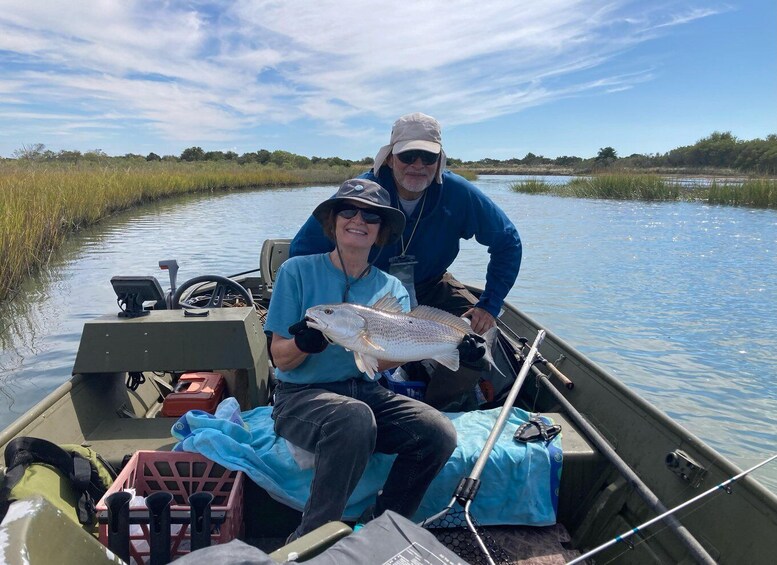 Two people on a boat holding a fish, surrounded by calm water and greenery. 4