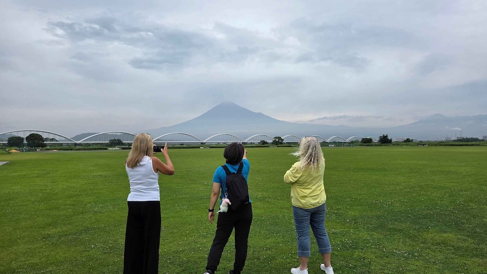 Three people taking a photo of a mountain with a bridge in the background. 4