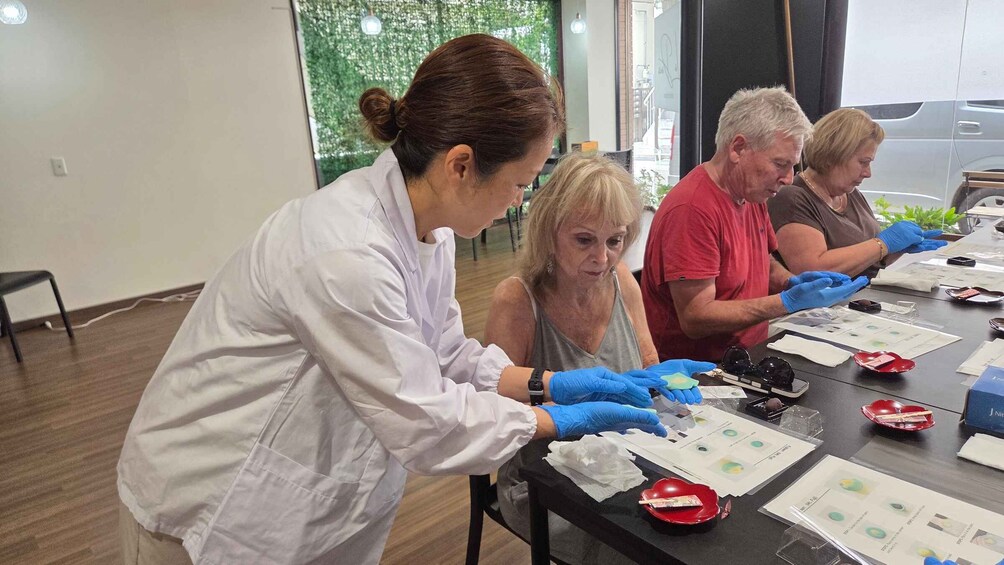 A group of people in a laboratory setting, wearing lab coats and gloves, working with scientific equipment and samples on a table. 3