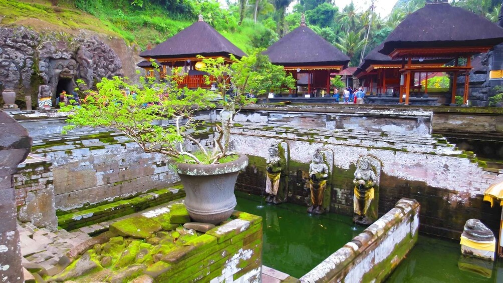 A traditional Balinese temple with stone carvings, a water feature, and thatched-roof structures. 2