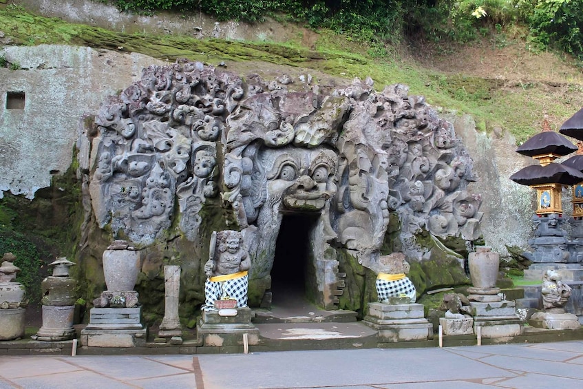 A stone entrance with intricate carvings, a small statue, and a traditional umbrella structure. 1