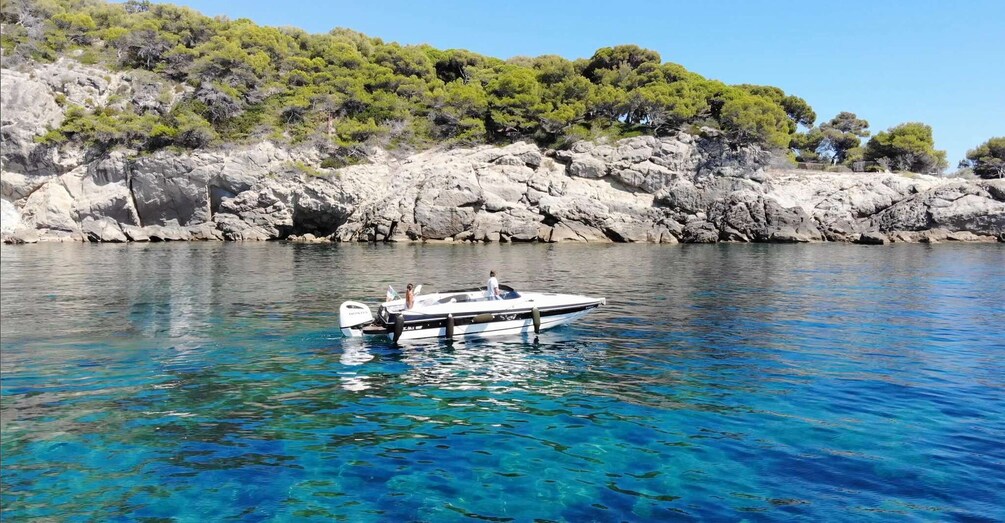 A boat on clear blue water with rocky cliffs and green trees in the background. 5
