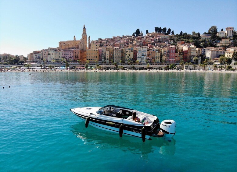 A boat on calm turquoise water with a coastal cityscape in the background. 1