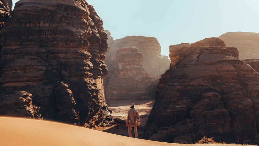A person standing on a sand dune with rock formations in the background. 1
