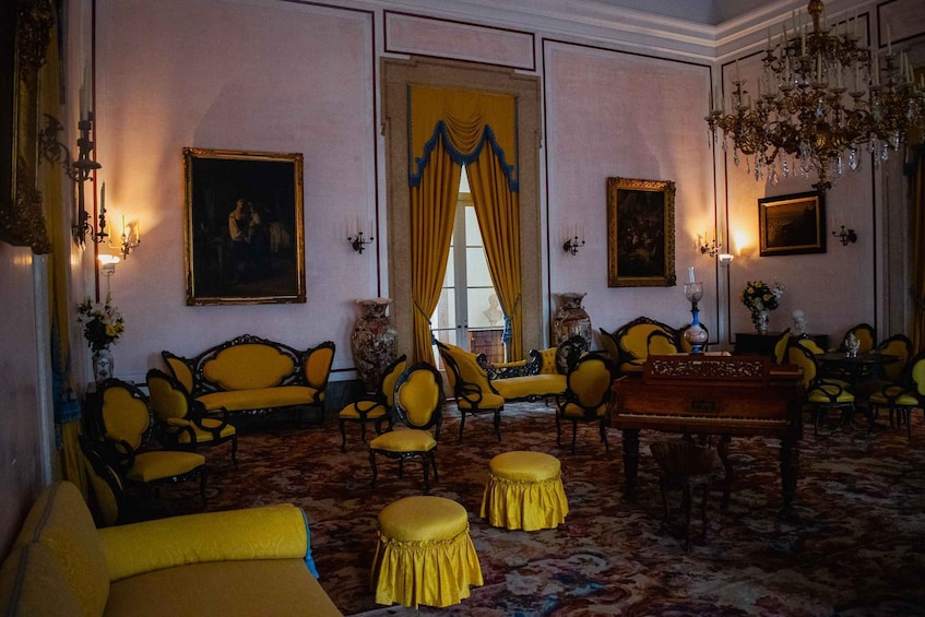 A room with yellow furniture, a piano, and paintings on the walls. 4