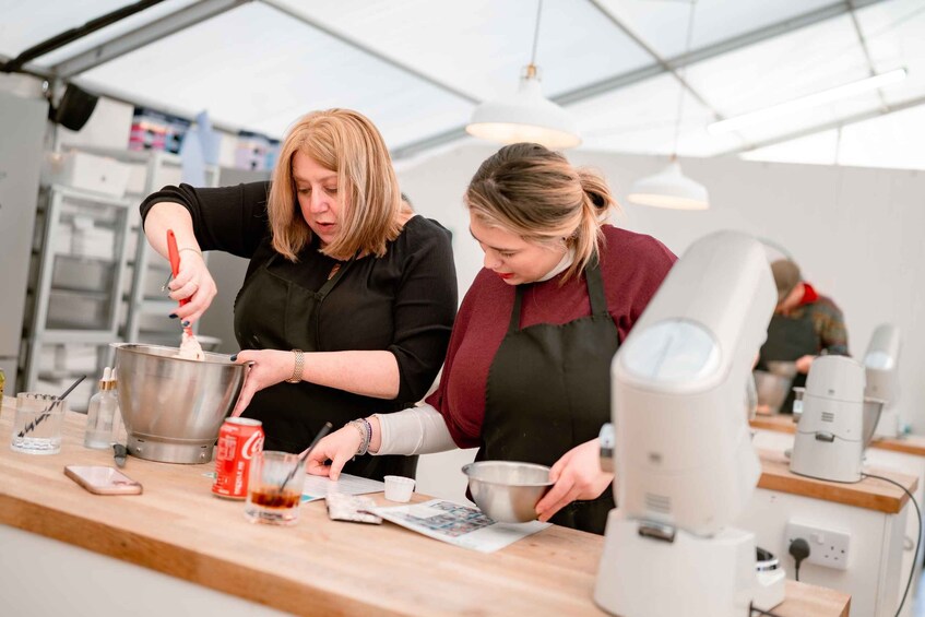Two people preparing food in a kitchen with a coffee machine and a soda can on the counter. 5