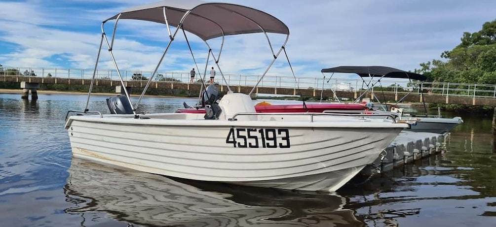 A white boat with the number 455193 on its side, docked at a pier with a bridge in the background. 1