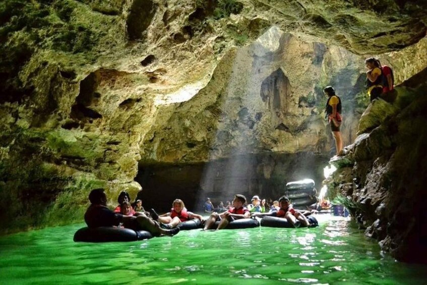 People floating on inner tubes in a cave with green water. 2