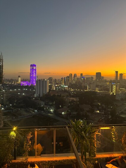 A city skyline at dusk with illuminated buildings and a sunset. 1