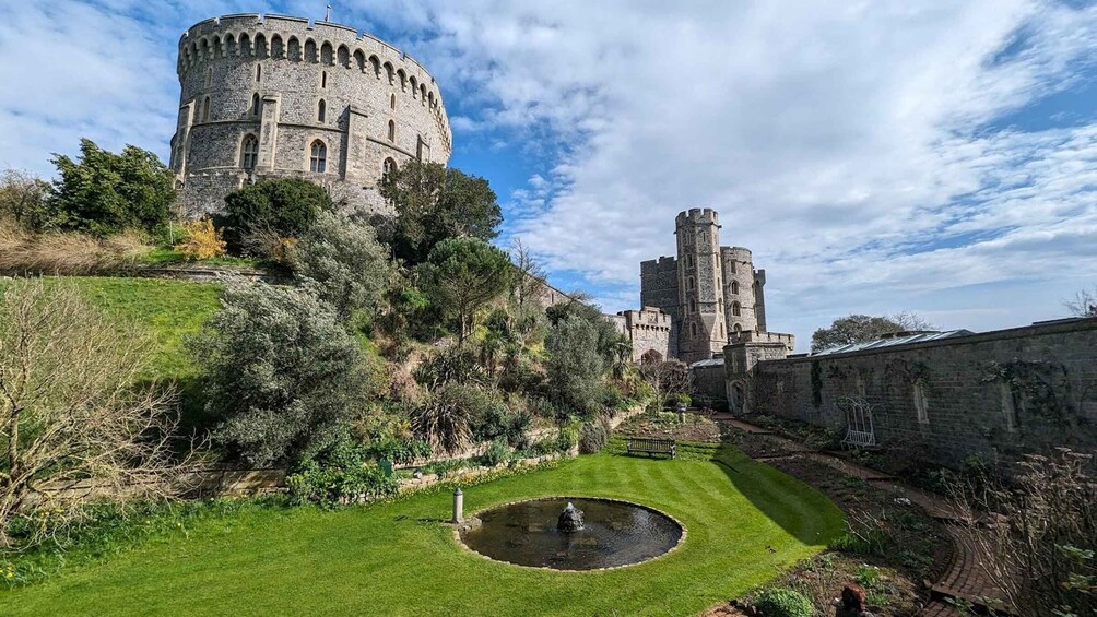 A historic castle with a round tower and a smaller tower, surrounded by lush greenery and a well-maintained lawn with a fountain. 5