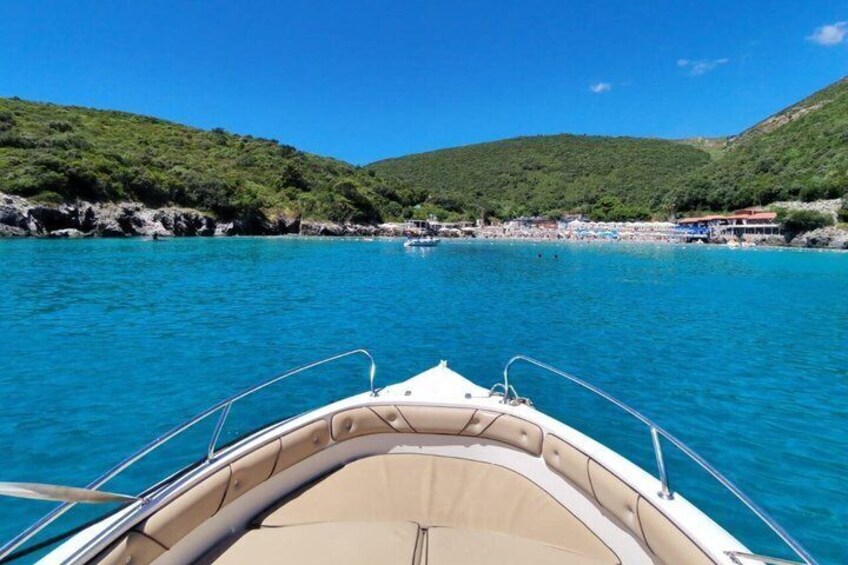 A boat on clear blue water with a green hillside in the background. 5