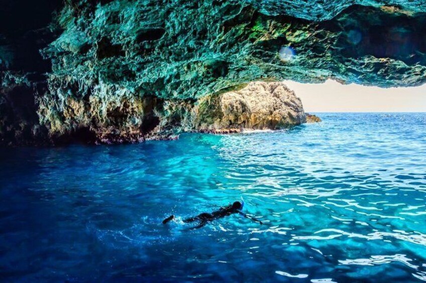 A swimmer in clear blue water under a rocky overhang. 1