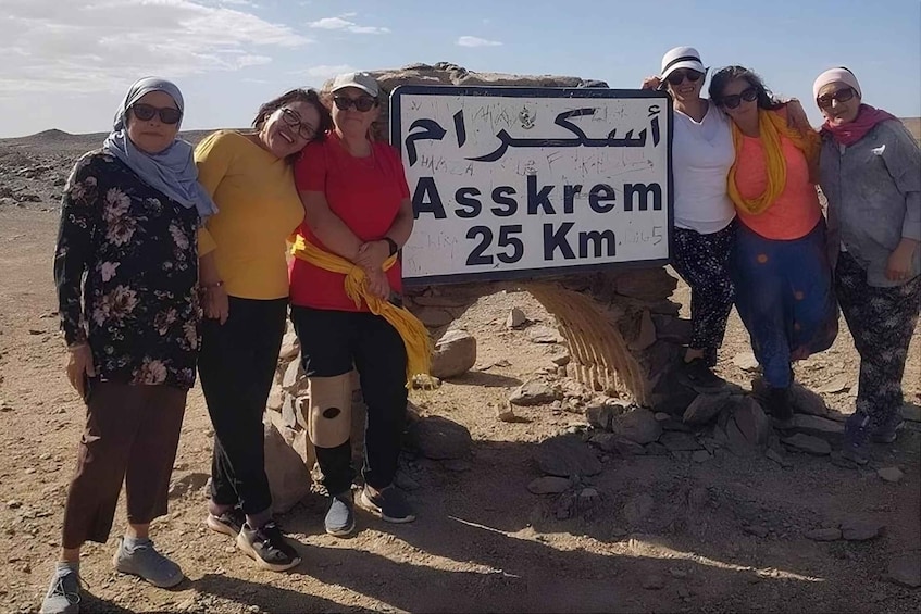 A group of people standing in a desert with a sign that reads 'Asskrem 25 Km.' 2